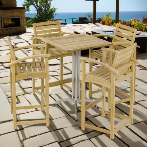 70635 Square Somerset Teak Dining Barstool Set of Somerset Square teak and stainless steel bar table and 4 Barstools angled on paver patio with trees and ocean and blue skies in  background