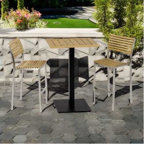 70640 Vogue 3 piece Bar Set showing 2 teak and stainless steel high bar stools and a rectangular bar table on stone terrace and landscape plants in background