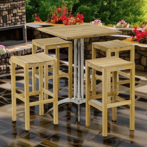 70646 Square Vogue Backless Barstool Set of a Vogue 30 inch square teak and stainless steel bar table and 4 Backless Barstools on stone patio with flowering plants and outdoor firepit in back