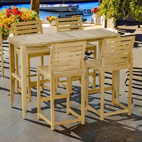 70649 Laguna Somerset Dining Set of Somerset teak rectangular table and 4  chairs angled on pavers surrounded by with flowering plants and shrubs with boat dock with 2 boats in background    