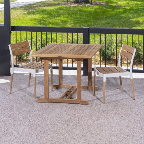 70653 Bloom teak and cast aluminum 3 piece Dinette Set on covered patio against a black railing lined with shrubs with grass lawn and walkway in background 