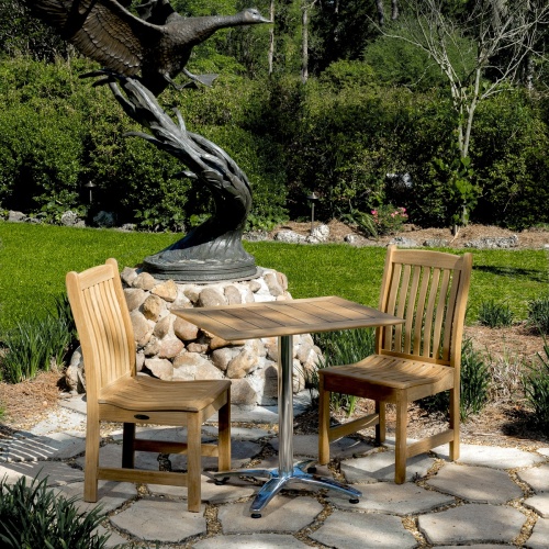 70669 Veranda Vogue Bistro Set of teak and stainless steel rectangular table and 2 teak dining chairs on stone patio with metal sculpture and trees in background