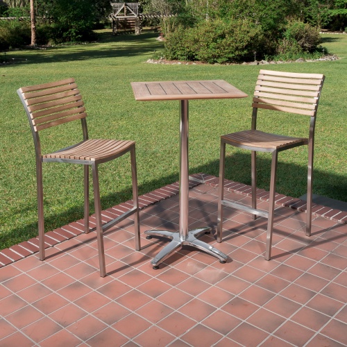 70673 Vogue teak and stainless steel High Bar Set of 2 barstools and 24 inch square teak table on brick paver and tiled outdoor patio with grass and landscape plants in background