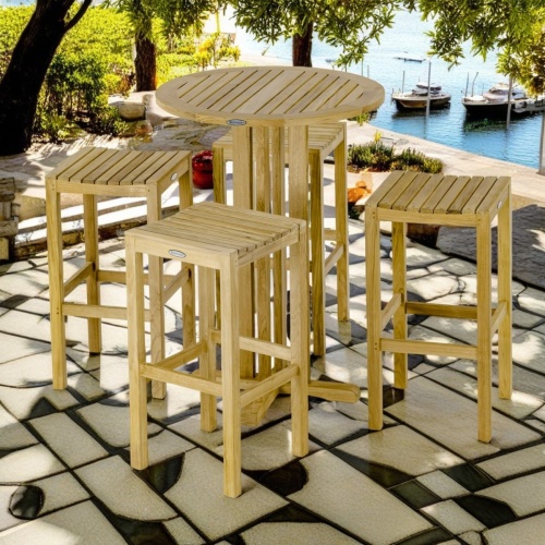 70681 Round Backless Teak High Top Dining Set of teak round 30 inch bar table and 4 backless barstools on concrete terrace surrounded by landscape plants with ocean and docked boats in background 