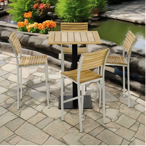 70687 Vogue 5 pc Bar Furniture Set of Vogue 30 inch square teak and stainless steel high bar table and 4 Vogue Side Chairs aerial view on paver patio with pond with shrubs in background