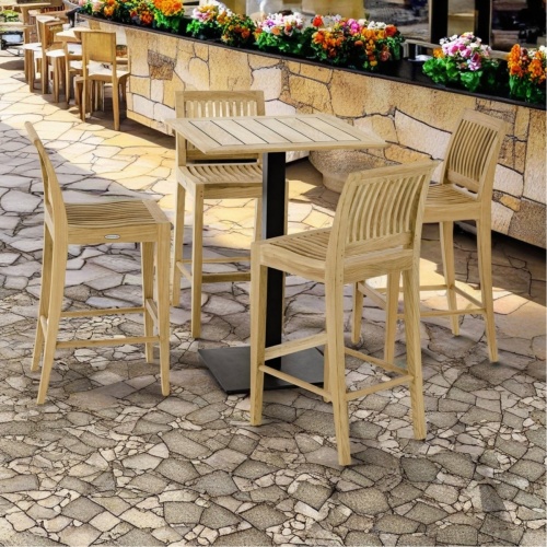 70691 Laguna Vogue 30 inch square teak bar table top and 4 side bar stools angled view on paver with paver planter with flowering plants in the background