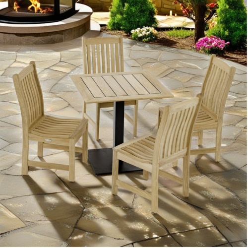 70699 Veranda 5pc Cafe Set of 4 teak dining side chairs and a 30 inch square teak dining table angled view on pavers with firepit and landscape trees in background