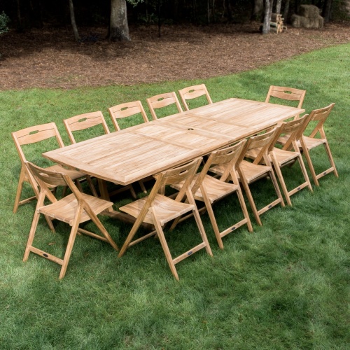 70731 Surf Valencia 13 piece teak rectangular Dining Set of a rectangular extension table and 12 teak dining chairs on grass with mulched area with trees in background