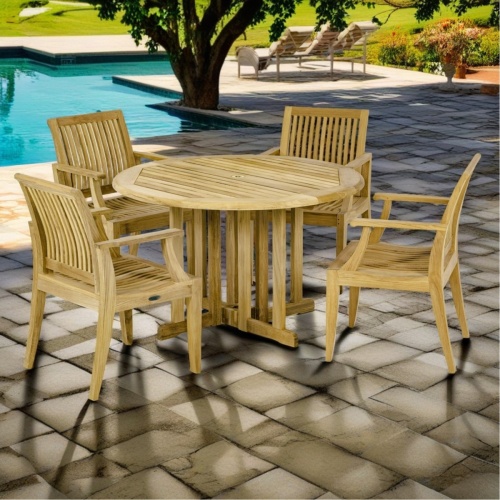 70736 Barbuda Laguna Dining Set of  Barbuda 48 inch round folding teak dining table and 4 Laguna Dining Chairs angled view on paver pool deck next to pool with grass lawn and plants in the background 