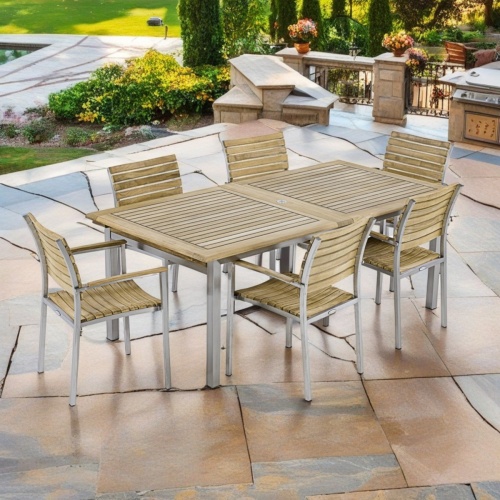 70756 Vogue teak and stainless steel 7 piece Armchair Dining Set of rectangular extendable dining table and 6 armchairs angled view on patio with trees and plants in the background