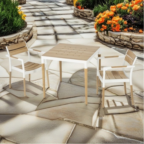 70761 Bloom 3 pc Dining Set of 2 teak and powdered coated aluminum armchairs and a 36 inch square bistro dining table on concrete patio and flowering shrubs in the background