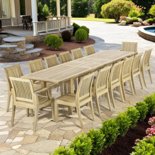 70770 Grand Laguna 15 pc rectangular teak dining Set of Extendable Teak Rectangular Dining Table and 12 Laguna dining side chairs and 2 Dining arm chairs on patio surrounded by plants  with fountain and home in background 