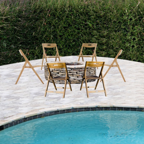 70782 Surf 6 piece Fire Pit Seating Set around stone fire pit on pool patio with pool in foreground and shrubs in background
