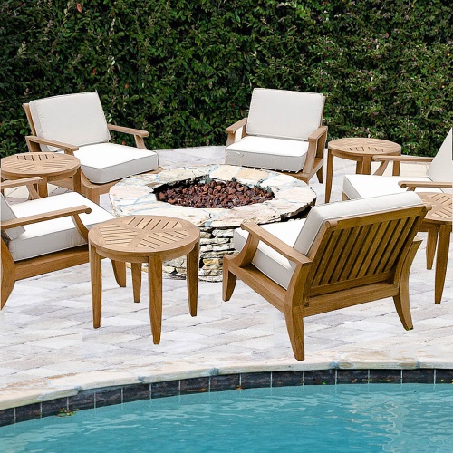 70784 Laguna 4 piece Armchair Firepit Deep Seating Set around a stone fire pit  and 3 teak side tables on a paver patio showing a pool in front of set and shrubs in background
