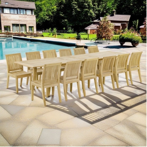 thumbnail image of 70810 Grand Laguna 15 piece teak Dining Set of 14 dining armchairs and rectangular 11 foot extendable dining table side angled on stone patio next to a pool with house and guesthouse in background
