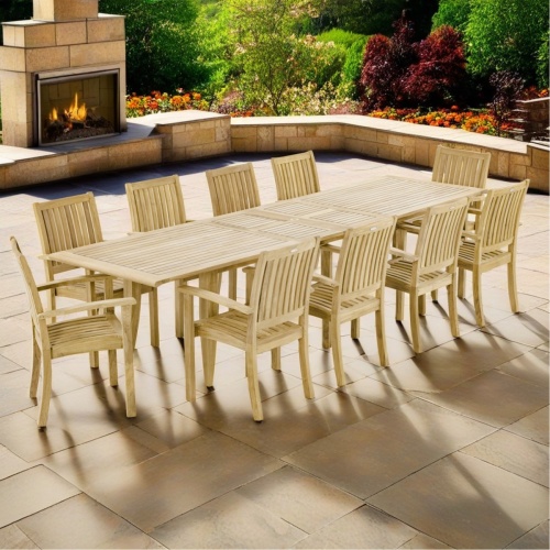 70812 Laguna Sussex teak 11 piece Dining Set of 10 teak armchairs and teak 11 foot extendable dining table side angle view on pavers with fireplace and flowering plants in background