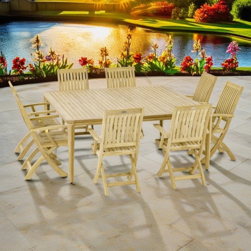 70813 Veranda Barbuda Dining Set for 8 on an outdoor stone patio with flowering plants in a row with a pond and shrubs in the background