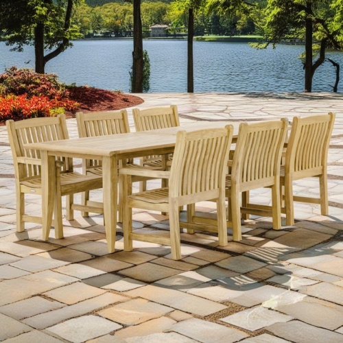 70815 Laguna Veranda 7 piece teak Dining Set of 6 teak dining armchairs and rectangular extendable dining table side angled view on stone patio overlooking a lake with homes in background