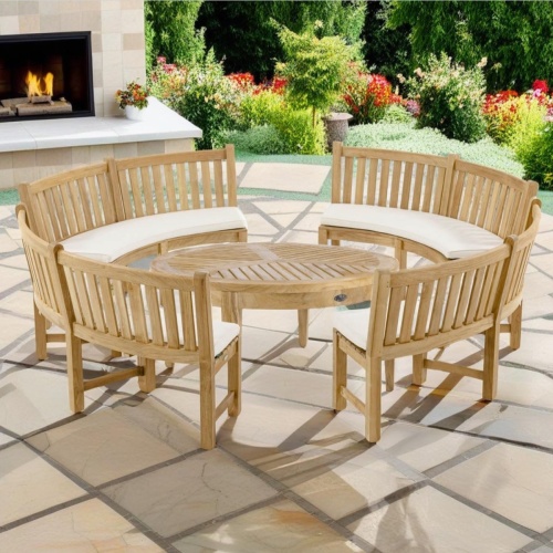 70862 Buckingham Bench and Coffee Table Set of 4 teak 6ft curved bench around a Laguna round coffee table on patio with a fireplace and landscaping plants in background 