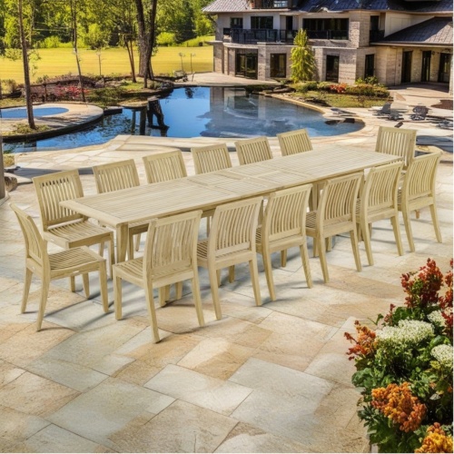  70917 Grand Laguna 15 piece teak Dining Set of 14 dining armchair and rectangular 11 foot extendable dining table side angled on pavers next to pool with mansion in background