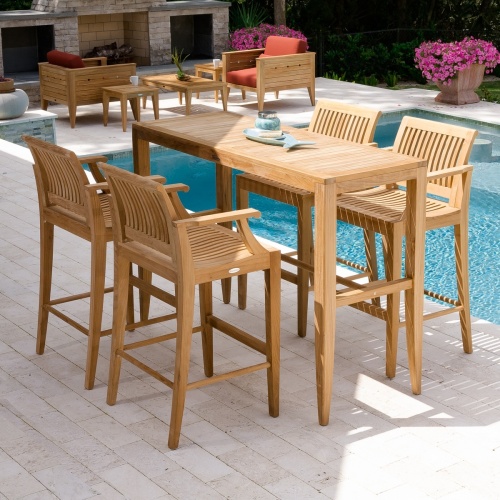 12910 Laguna barstool with 5 piece Teak High Bar Set on outdoor patio showing fish plate and candle holder on table by pool with fireplace two flowering potted plants and shrubs in background 