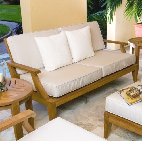 13152dp laguna teak loveseat collection set angled on outdoor patio with candle and holder open magazine potted palm tree with landscaped background