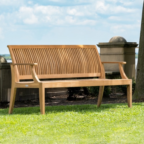 13811ph Laguna 6 foot teak bench on grass with low concrete wall and tree trunk and blue sky in background