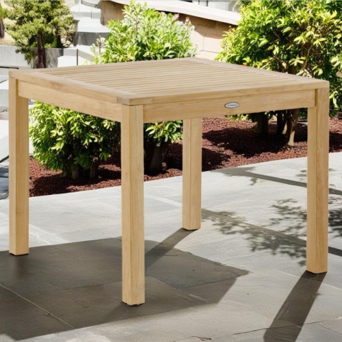 15005 Teak Square table angled view on patio with landscape plants in background