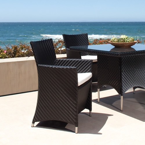 29001BKDP Valencia Black Armchair with dining set showing decorative bowl on table top on a concrete terrace surrounded by landscape plants with ocean and blue sky background