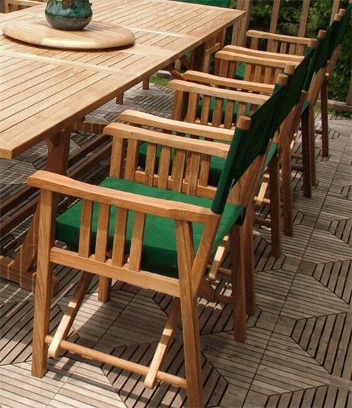 70006 Veranda teak 11 piece dining set close angled view of director chairs plant on teak lazy susan on teak floor deck with trees in background