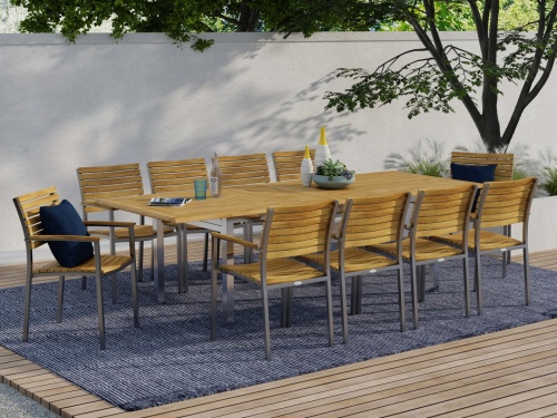 70055 Vogue 11 piece Dining Set with magazines and drinking glass and vases with potted plant on top in an angled side view on outdoor wood patio on area rug with privacy wall in back