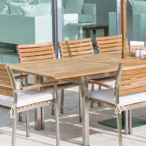 70055 Vogue 11 piece teak and 304 stainless steel dining set with optional seat cushions salt and pepper shakers napkin holder on outdoor lanai with glass doors in background