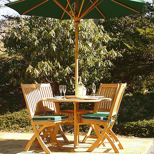 70056 Hyatt Barbuda teak 5 piece Dining Set showing 4 place settings and wine glasses bottle of wine on table with optional open market umbrella on teak tiles with shrubs in background