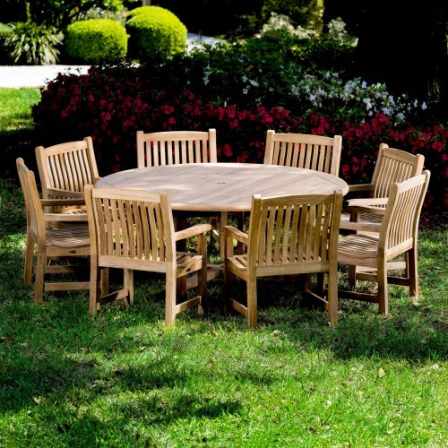 70173 Buckingham nine piece teak Dining Set with six foot diameter dining table and 8 dining chairs on grass lawn with flowers and tree landscape in background