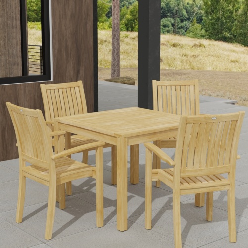 70210 Sussex 5 pc Teak Dining Set of Square Bistro Teak Table and 4 Sussex Armchairs in angled corner view on patio of house next to windows with grass and trees in the background