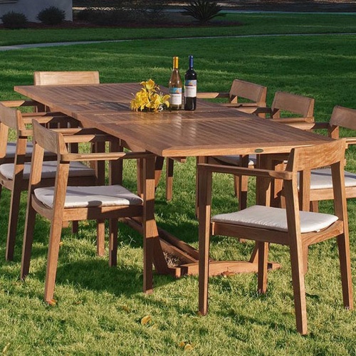 70237 Grand Horizon teak 9 piece Dining Set with optional canvas colored cushions with yellow flowers two wine bottles on grass lawn house and landscaped background