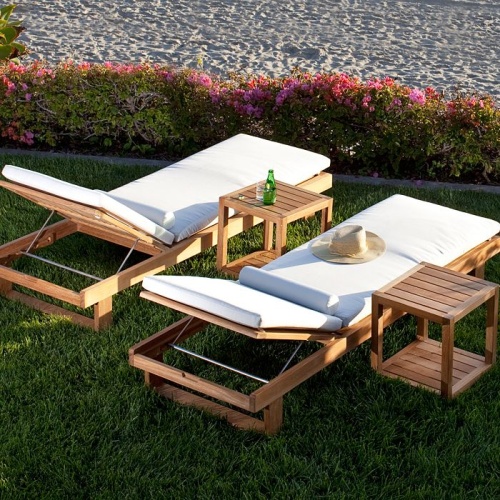 70308 Horizon teak double chaise set cushioned with hat on one and two side tables with a bottle water and glass set angled on lawn with flowering plants and sand in background
