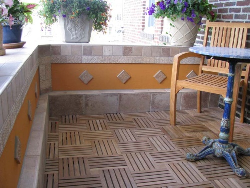 70409 parquet teak tiles assembled on a condo balcony with four potted flowering plants on travertine tiled concrete railing with chair and table on teak tiles