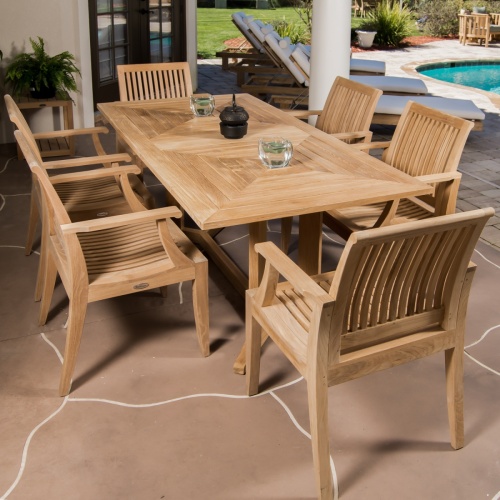 70422 Pyramid 7 piece Teak Dining Set on covered patio shown with 2 glass candle holders with candles black tea pot with patio doors plants loungers and pool in background
