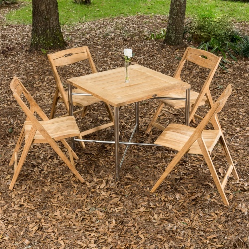 70450 Surf Odyssey folding Dining Set of Odyssey 32 inch square table with bud vase and 4 Surf teak folding dining chairs on mulch area with trees and grass in background