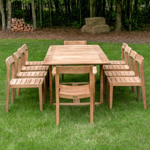  70457 Horizon eleven piece teak Dining Set outdoors end view on grass lawn with trees and shrubs in background