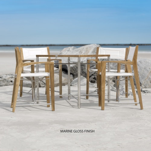 70459 Odyssey 5 Piece folding teak and stainless steel dining set of Odyssey 32 inch square dining table and 4 Odyssey folding chairs on beach with ocean and sky in background