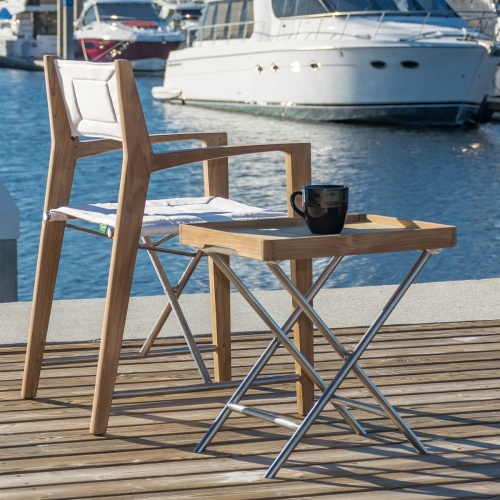 70461 odyssey teak and stainless steel folding chair and ottoman side table with coffee cup with boats and water in background with coffee cup with boats and water in background
