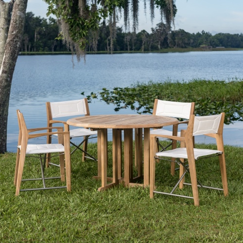 70473 Odyssey Barbuda 5 piece Folding Dining Set of 4 folding director chairs and a 48 inch round teak table on grass with palm trees overlooking blue lake