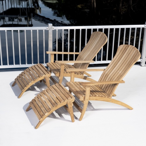 70509 Double Adirondack Set of 2 teak chairs and 2 teak foot rests on concrete patio side view showing metal balcony rail trees boathouse dock and water in background 