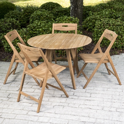 70519 Surf 5 piece teak round Dining Set on brick paver patio with landscaped bushes trees and grass in background