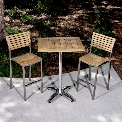 70667 Vogue Rectangular teak and stainless steel Bar Set of 2 barstools and rectangular teak dining table on concrete patio with landscape shrubs background