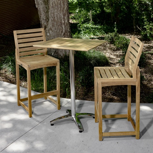 70676 Somerset 3 piece Rectangular Barstool Bar Set of 2 teak barstools and a teak and stainless steel rectangular bar table on concrete patio and trees and plants in background
