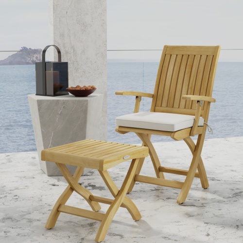 70799 Barbuda Chair and Ottoman Set showing Barbuda Chair with optional seat cushion and Ottoman in angled side view next to table with candle holder and bowl with ocean in back