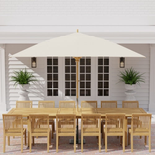 70810 Laguna 13 pc Teak Dining Set in side profile with optional umbrella and 2 potted plants on pillars with door in center and house in the background